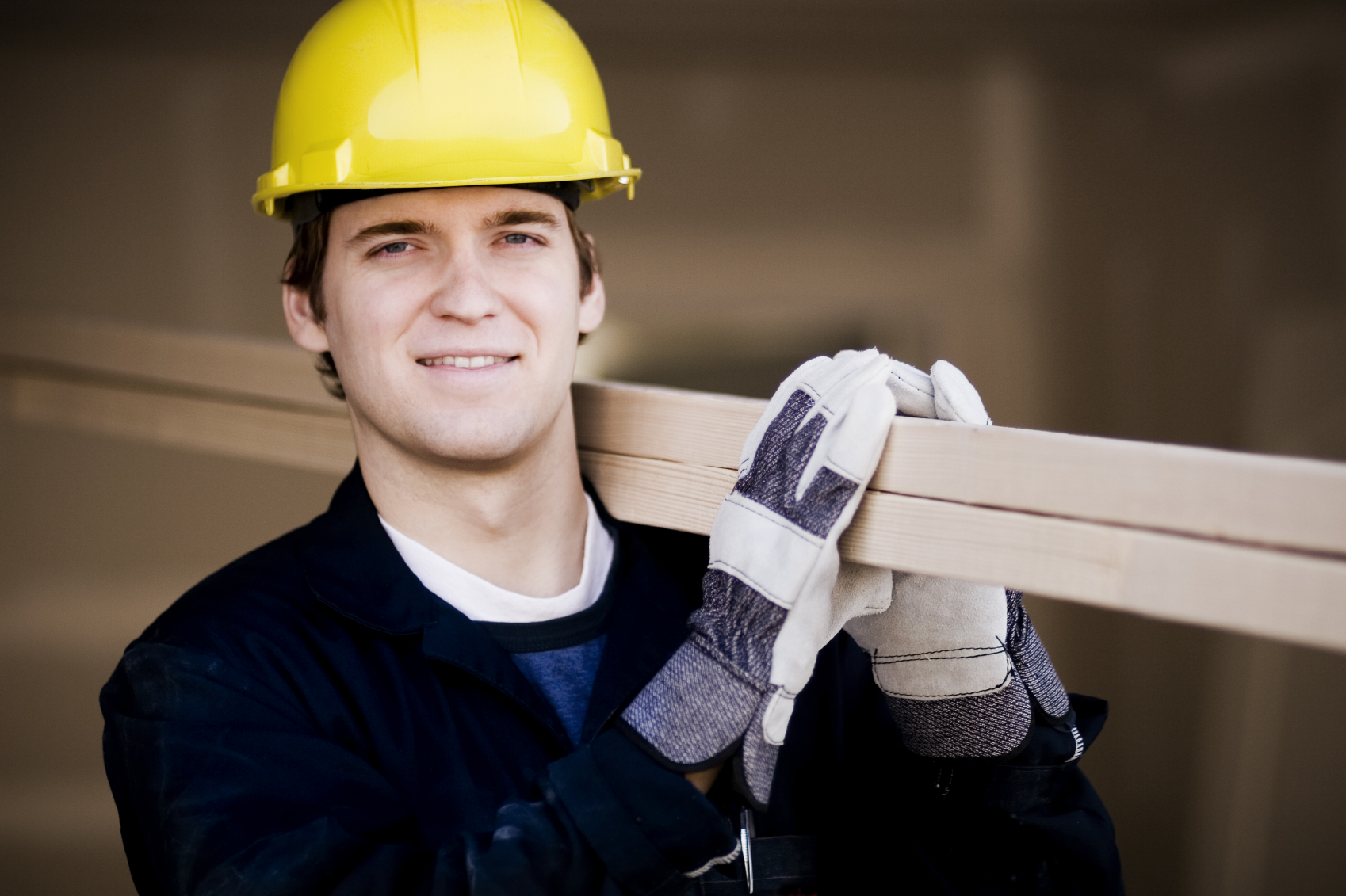 Construction worker in a yellow hard hat carrying lumber.